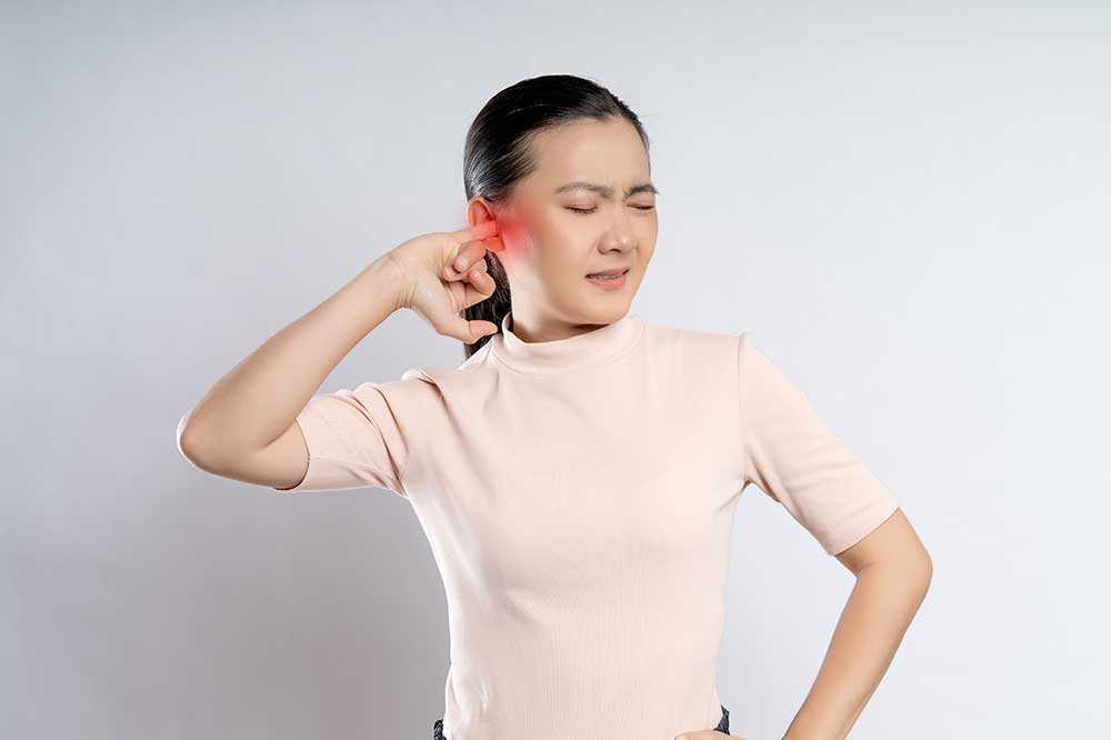 A woman with a pained expression holds her finger to her ear, which is highlighted in red to indicate pain or infection.